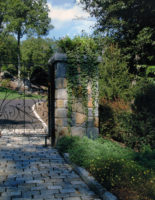 This custom designed front entry was constructed for a client in South Salem, NY. The fieldstone columns are topped with massive 4” bluestone caps and softened with elegant planters filled with cascading flowers and foliage. The distinctive black wrought iron gates were custom designed in concert with the client. 