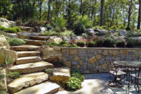  	With limited space on a very steeply sloped yard, we carved out a little bit of heaven for the owners of this Scarsdale home, constructing an elegant bluestone terrace, surrounded by a fieldstone retaining wall with rock face bluestone cap and featuring a built-in grill that the owners use year-round. These natural steps work beautifully with the more formal patio, allowing the homeowners to move seamlessly from the main house to the upper yard. Note the plantings on the hillside which enhance and beautify the hillside year-round. 