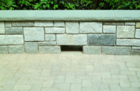 This grey stone terrace, in Redding, CT, is flanked by a fieldstone sitting wall with a rock face bluestone cap. The large weep hole at the base allows water to drain off with ease.